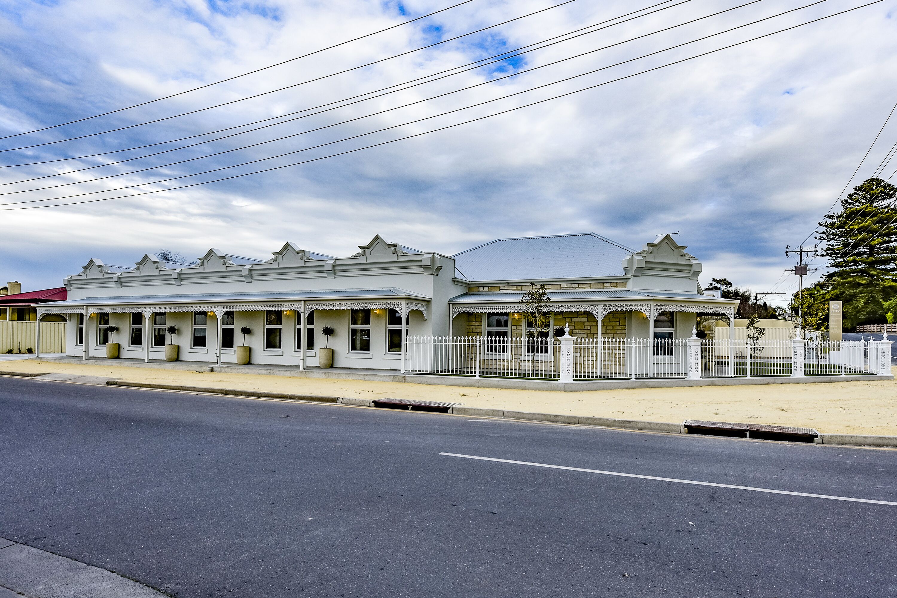 A white building with a symmetrical facade, large windows, and a white fence.
