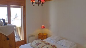 Ein Schlafzimmer mit einem Bett, einem Nachttisch mit Lampe, einem Heizgerät und einem Fenster mit Blick auf Bäume.