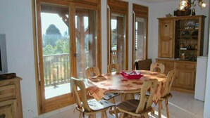 Ein Essbereich mit Holztisch und -stühlen, eine Küche mit Holzschränken und ein Balkon mit Blick.
