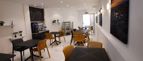 Un comedor moderno con mesas y sillas, una zona de cocina y obras de arte en las paredes.