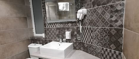 Un baño moderno con un lavabo blanco, inodoro y un secador de pelo montado en la pared.