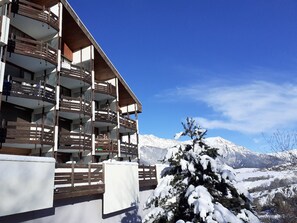 A multi-story building with balconies, a snow-covered tree, and a mountainous backdrop. - Charming studio for 4 in Sauze with balcony and parking (Enchastrayes)