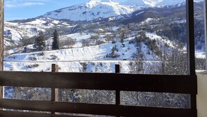 Vista a través de una ventana con marco de madera, mostrando un paisaje montañoso nevado con cielo despejado.