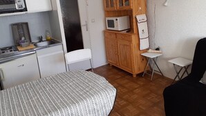 Habitación compacta con kitchenette, una cama, un armario de madera, un televisor y una mesita.