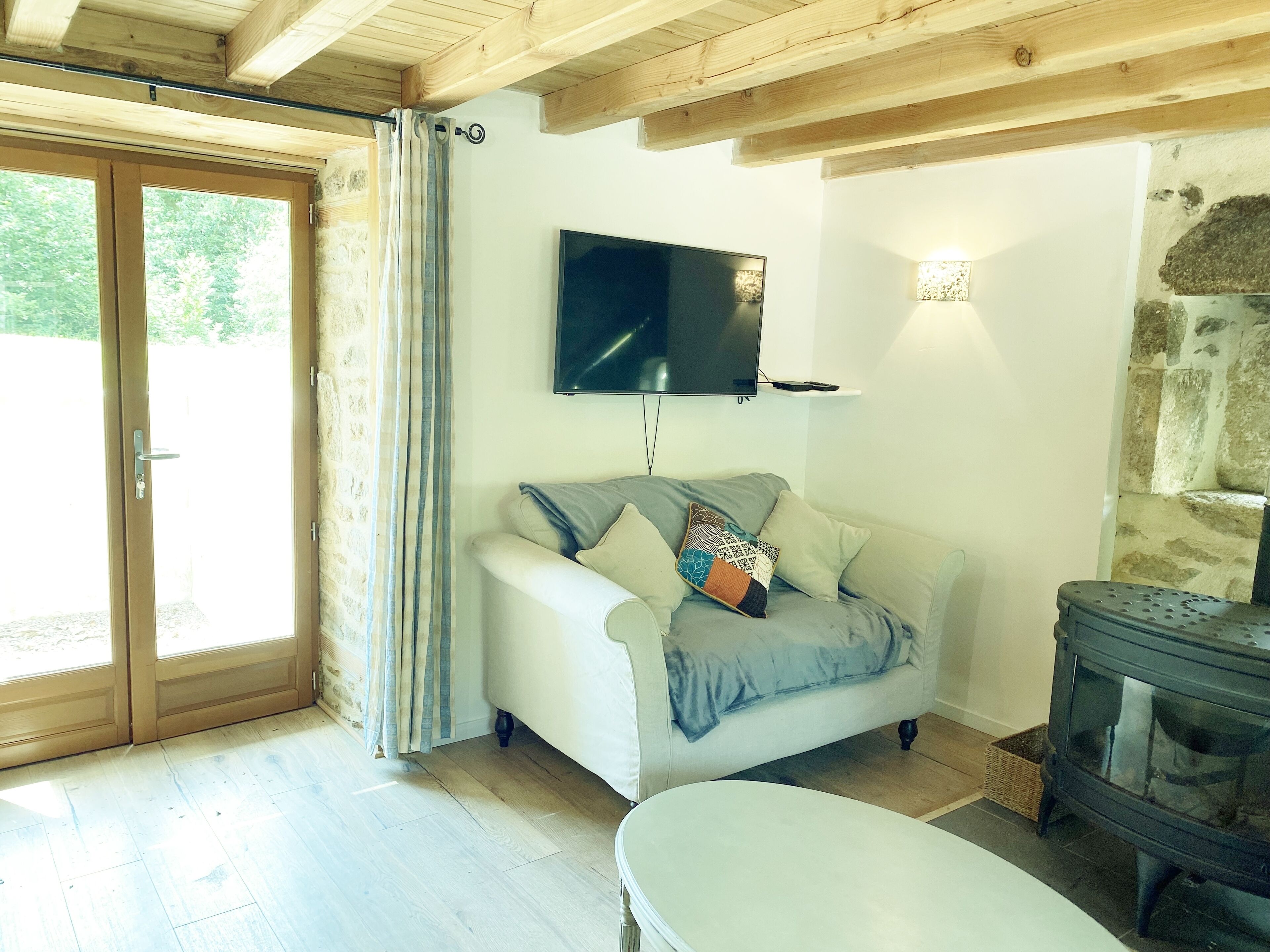 A cozy living room with a sofa, a flat-screen TV, a stone wall, and a wooden ceiling.