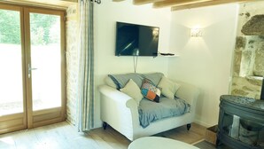 A cozy living room with a sofa, a flat-screen TV, a stone wall, and a wooden ceiling. - The perfect Couple's Retreat (Abjat-sur-Bandiat)