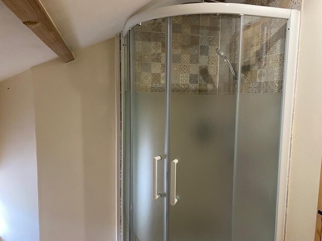 A glass-enclosed shower area with a tiled backsplash and a white ceiling.