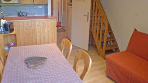 A compact kitchen with wooden cabinets, a microwave, and a toaster. There's a dining table with a checkered tablecloth and a large knife on it. A wooden chair is visible, and there's a red cushion on the floor. - Apartment for 5 with private balcony and parking in Samoëns (Samoëns)