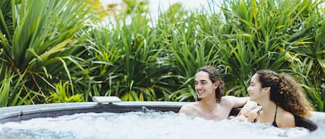 A hot tub with two people in it, surrounded by lush greenery.