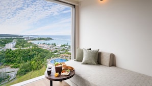 A balcony with a view of a coastal town, a dining table with food and drinks, and a sofa with cushions. - Oriental Hotel Okinawa Resort & Spa (Nago)