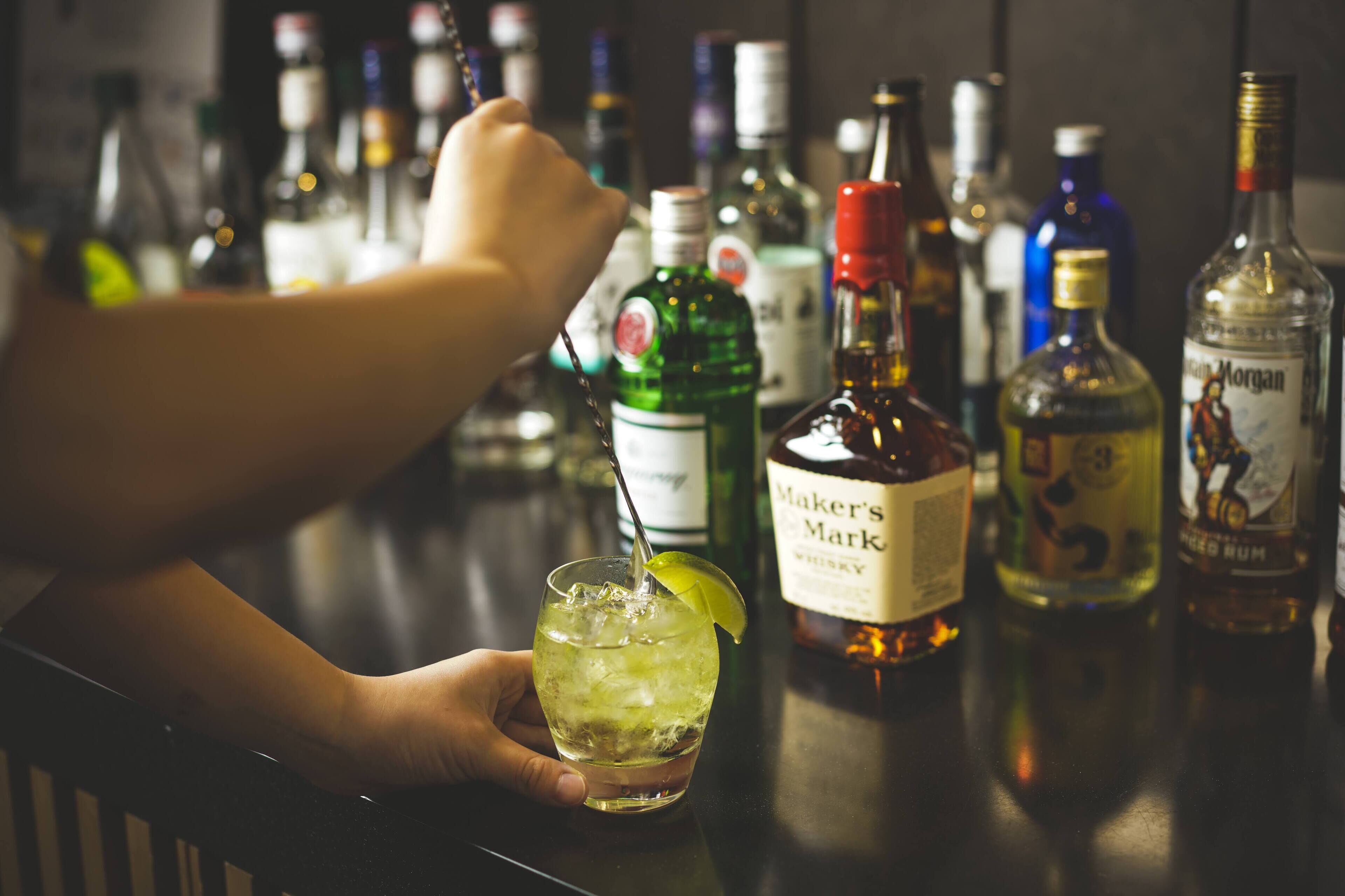 A bar setting with various liquor bottles and a hand holding a cocktail glass.