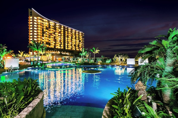 Um hotel com uma grande área de piscina, cercado por palmeiras e caminhos bem iluminados.