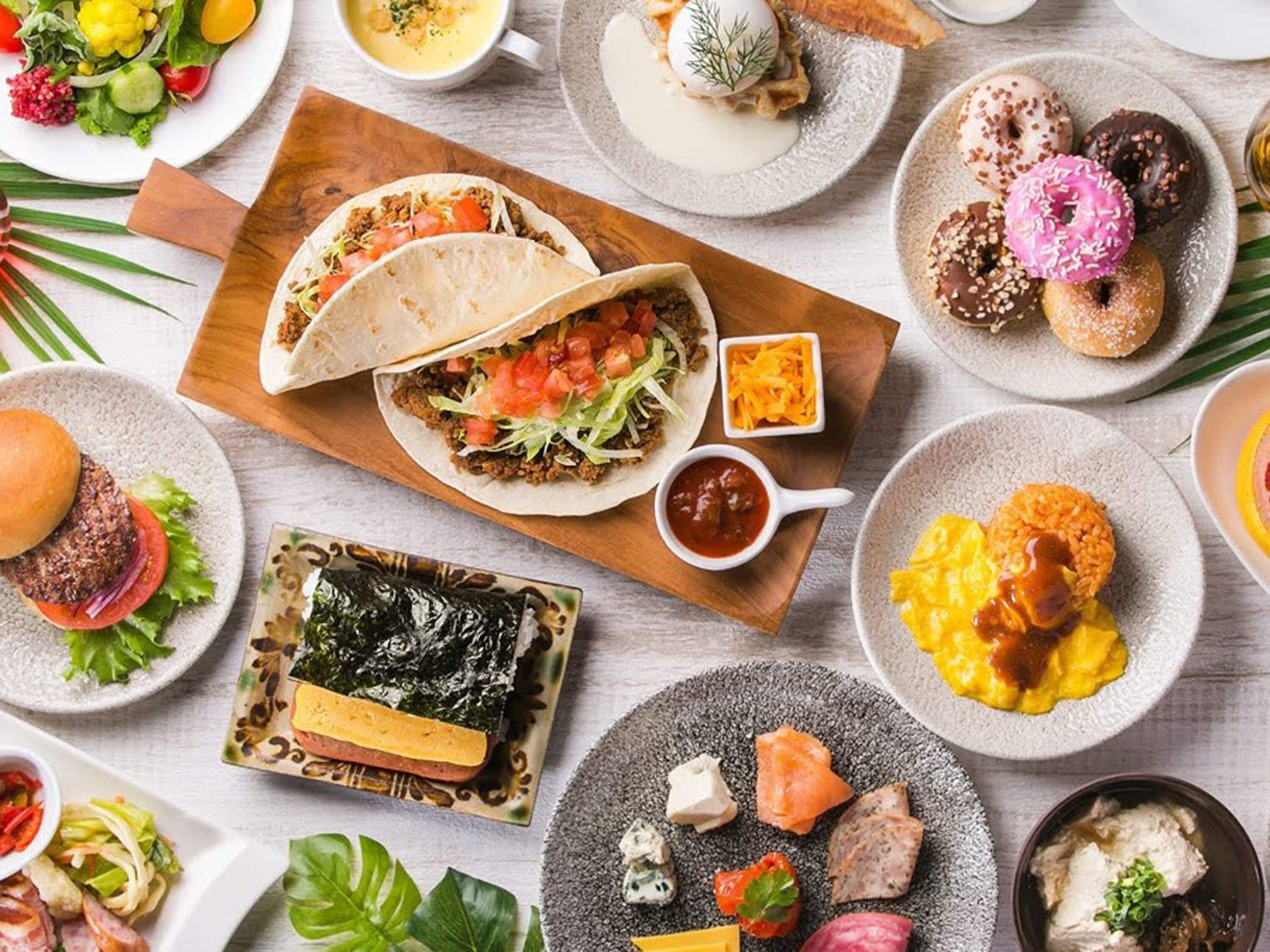 A variety of dishes including tacos, a burger, and a plate of sushi.