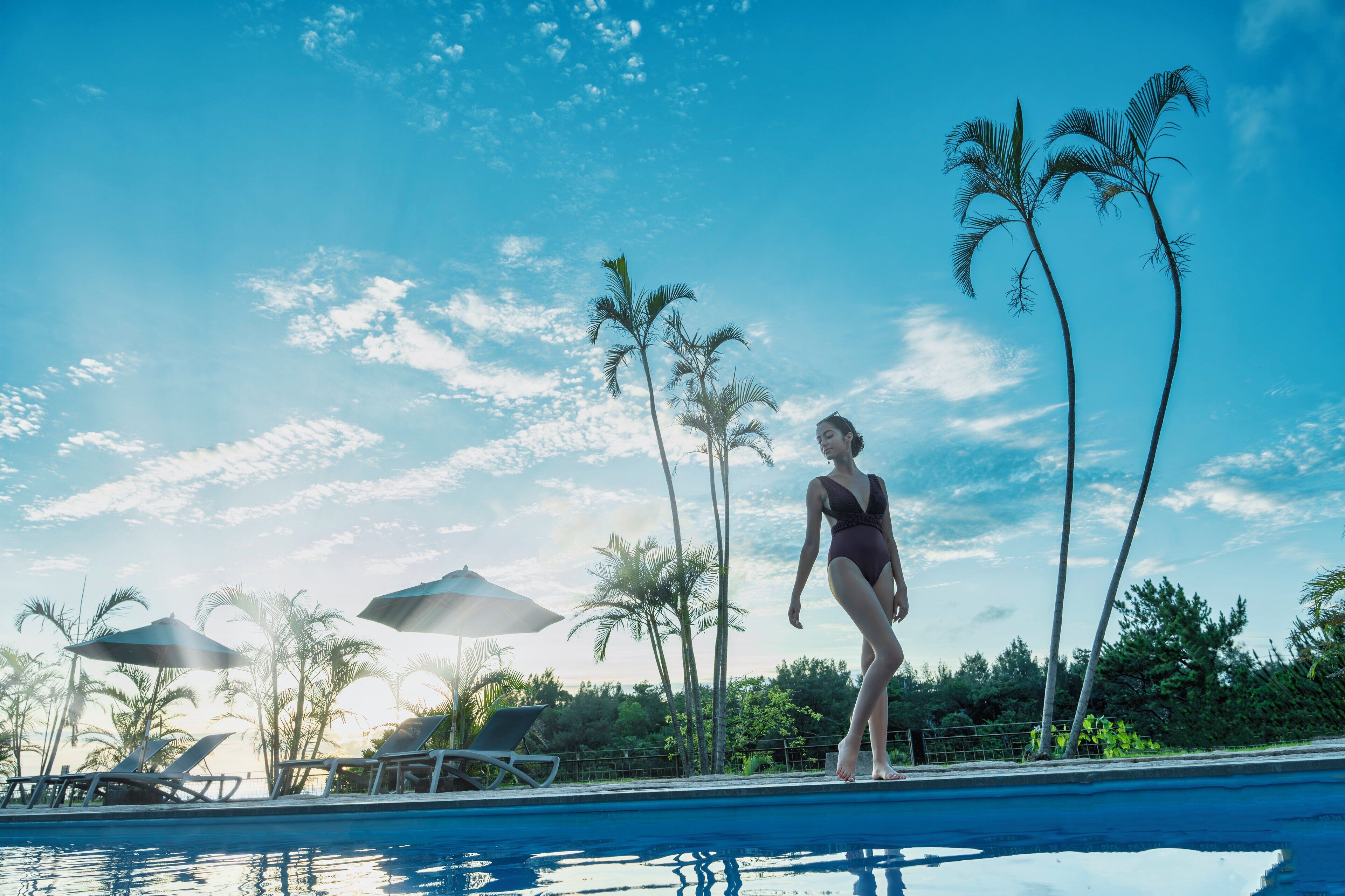 A pool area with lounge chairs and umbrellas, surrounded by palm trees.