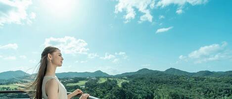 A person standing on a balcony with a view of a forested landscape and mountains.