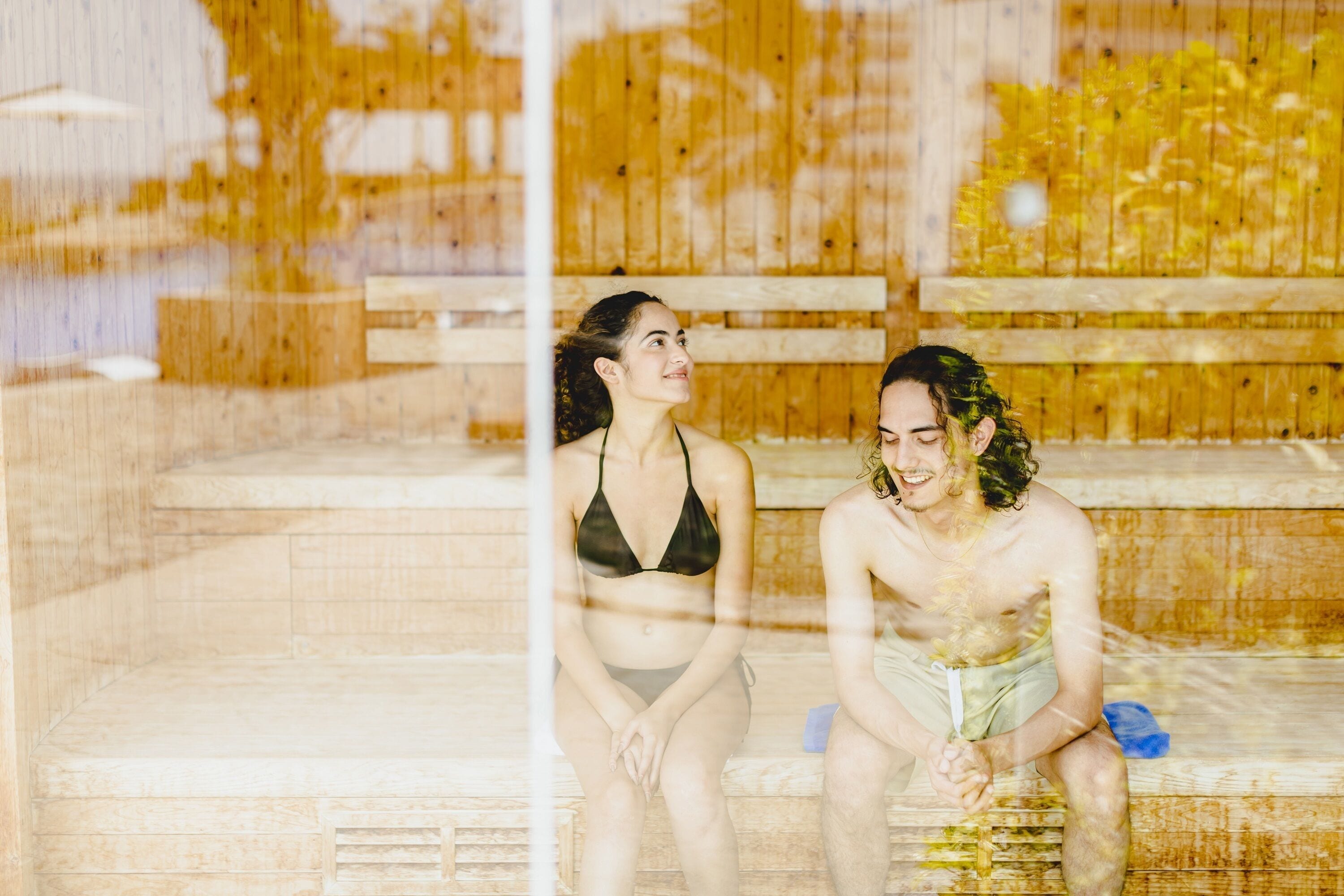 Two people sitting on wooden benches in a wooden cabin-like setting.