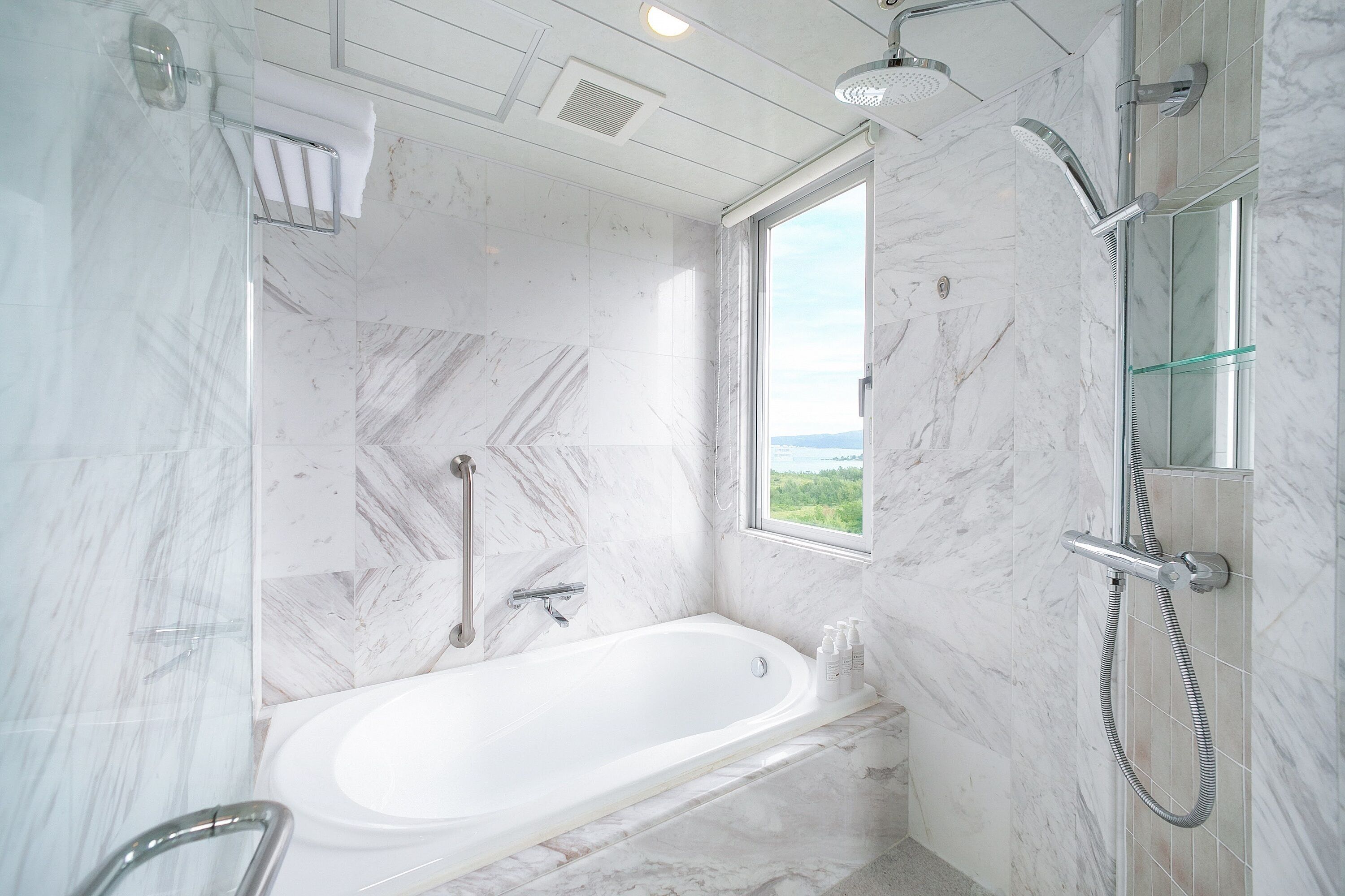A modern bathroom with a bathtub, shower, and a window providing a view.