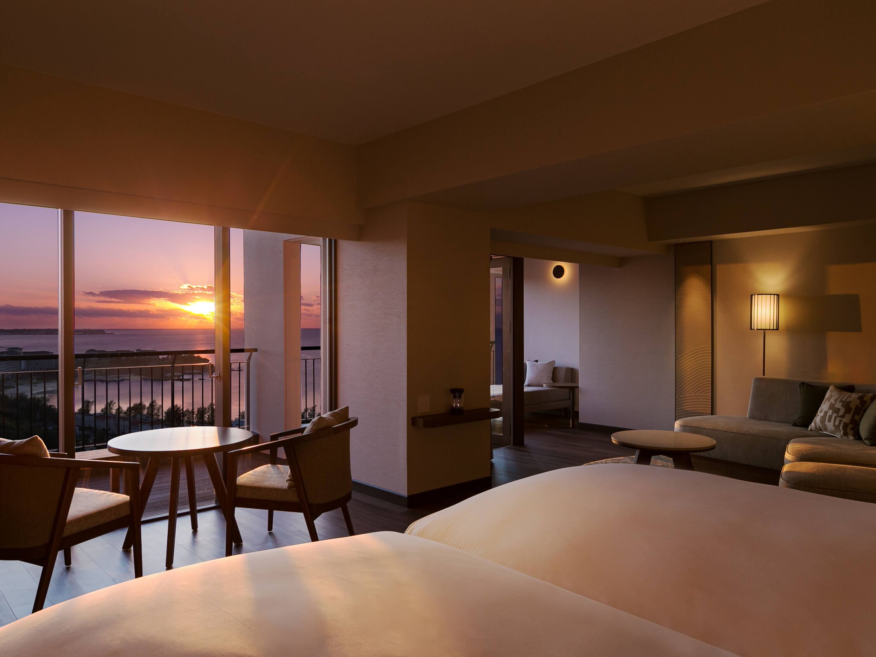 A hotel room with a balcony, a sofa, a dining table, and a chair.