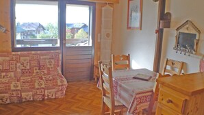 Een gezellige kamer met een houten vloer, een gestreept bankje, een eettafel met stoelen en een raam met uitzicht op huizen.