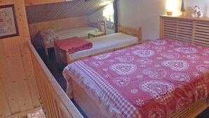 Een knus ingerichte kamer met een schuine kap, houten wanden en een bed met een beddeken met een patroon.