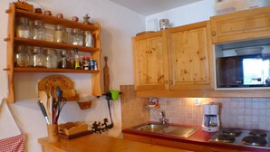 Een keuken met houten kastjes, een roestvrijstalen spoelbak, een koffiezetapparaat en een magnetron.