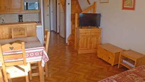 Een gezellige woonruimte met een houten eettafel, stoelen, een televisie op een houten kast en een keuken op de achtergrond.