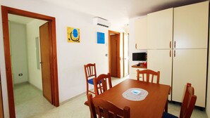 A dining area with a wooden table and chairs, a television, and a refrigerator.