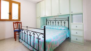 A bedroom with a metal bed frame, a wooden chair, a window, and light green cabinets.