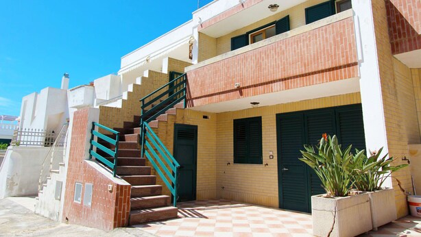 A two-story building with a staircase leading to the upper floor, a door with a window, and a potted plant in the foreground.