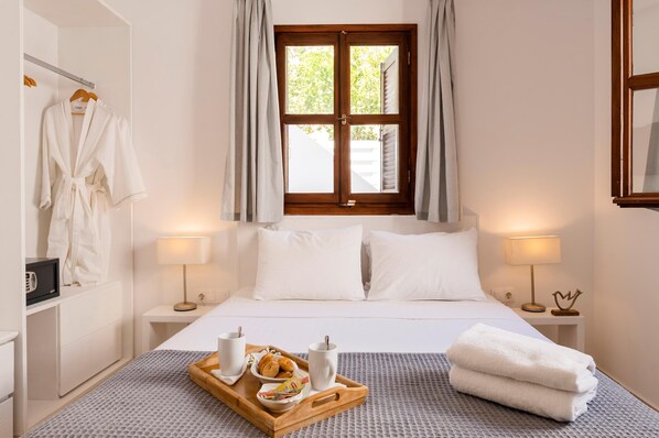 Hotelkamer met een bed, twee nachtkastjes met lampen, een raam met gordijnen, een badjas hangend aan een rek, en een dienblad met ontbijtartikelen.