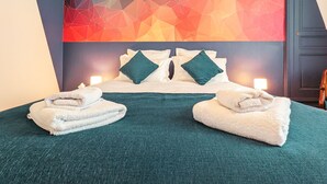Ein Hotelzimmer mit einem Bett, zwei Kissen, einer türkisblauen Tagesdecke und einem geometrischen Wandbild.