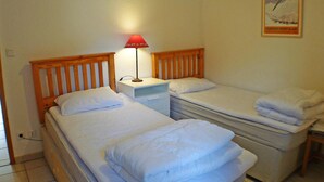 Una habitación con dos camas individuales, una mesita de noche con lámpara y un cartel en la pared.