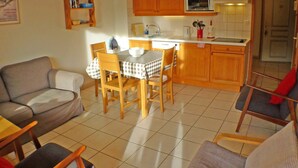 Cocina compacta con armarios de madera, un microondas y un lavamanos. Hay una mesa de comedor con sillas y un sofá en la sala de estar.