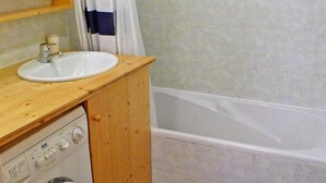 Un baño con tocador de madera, lavamanos, lavadora y bañera.