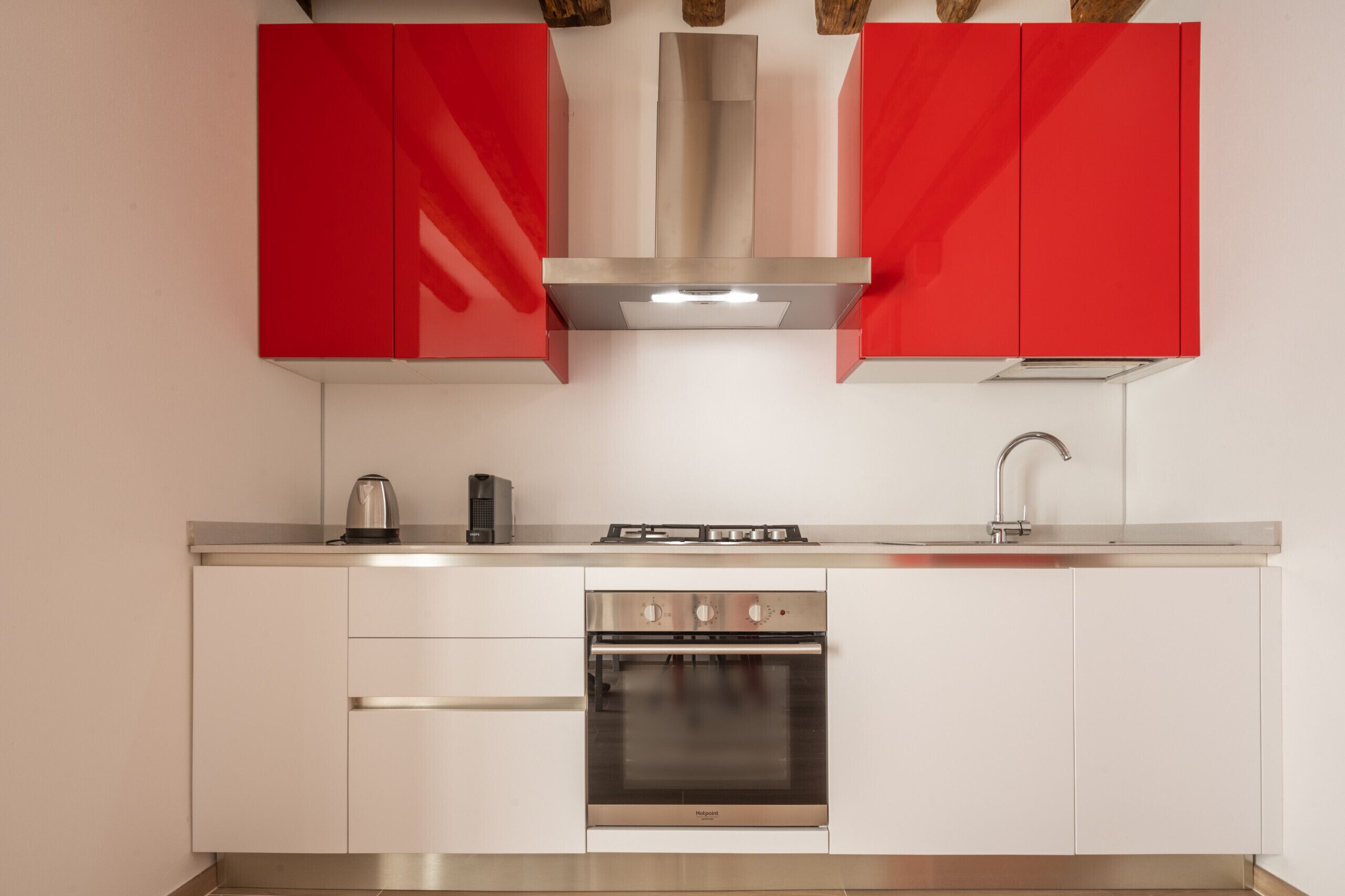 A kitchen with white cabinets, a stainless steel oven, and a red backsplash.