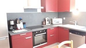 Eine kleine Küche mit roten Schränken, einem schwarzen Backofen, einer Kaffeemaschine, einem Toaster und einem Geschirrspüler.