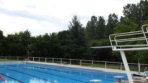 Ein Schwimmbecken mit Sprungbrettern, Liegestühlen und einem eingezäunten Bereich.