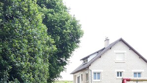 Ein Rasenstück mit Schaukel und einem Haus aus Stein mit Schornstein, sowie ein gepflasterter Weg.