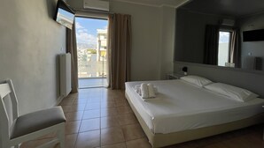 Une chambre d’hôtel avec un lit, une chaise, un téléviseur fixé au mur et une fenêtre avec des rideaux.