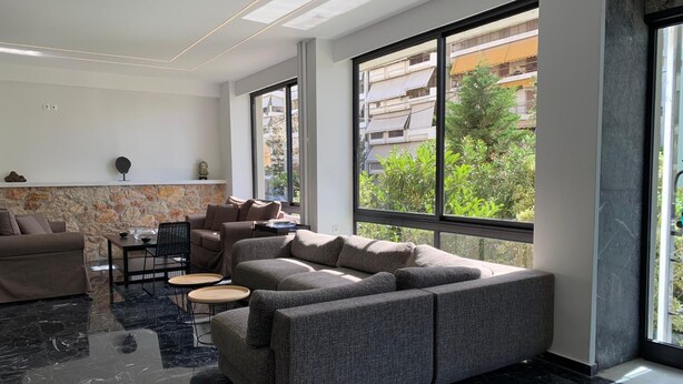 Un salon moderne avec un canapé d’angle, un coin repas comprenant une table et des chaises, et de grandes fenêtres offrant une vue sur la ville.