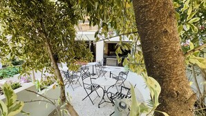 Un espace extérieur aménagé avec des chaises et des tables en métal, entouré de verdure et avec un bâtiment en arrière-plan.