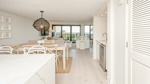 A modern kitchen with white cabinetry, a dining area with a white table and chairs, and a large window overlooking a balcony.