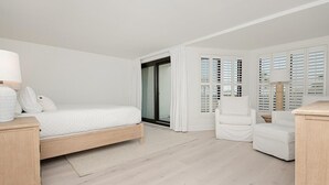 A modern bedroom with a wooden bed, white curtains, and a view through a glass door.