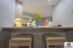 A kitchen with a microwave, a sink, and a vase with flowers on the counter. There are two wooden stools in front of the counter.