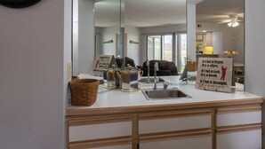 A kitchen with a sink, a mirror, and a clock on the wall.