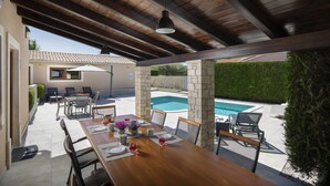 Un espace de restauration en plein air avec une table en bois prévue pour quatre personnes, entourée de chaises, à proximité d’une piscine.