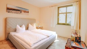 A neatly made bed with a quilted headboard, a bedside table with a lamp, and a window with curtains.