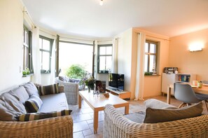 A cozy living room with a sofa, a coffee table, and a TV. There are wicker chairs and a dining table with chairs. - Erdgeschosswohnung Am Leuchtfeuer Whg. LF 7.1 (Ostseebad Wustrow)