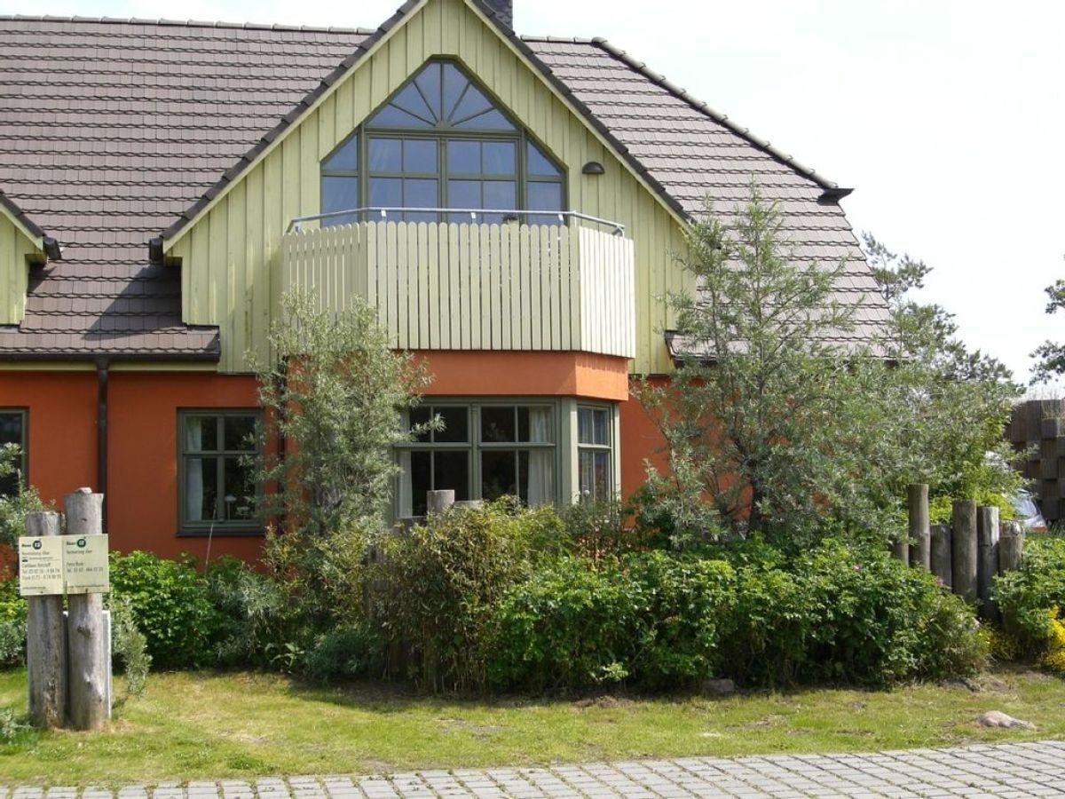 A two-story house with a sloped roof, a balcony, and a garden area with bushes and a wooden fence.