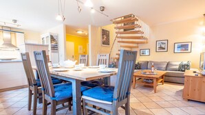 Uma área de refeições com uma mesa e cadeiras de madeira, um sofá e uma escada.